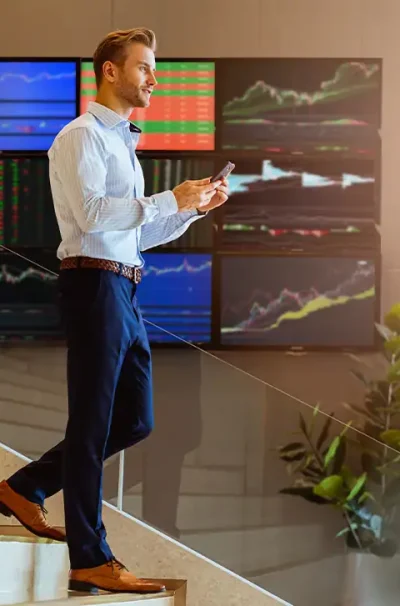Professional businessman checking phone in modern Dubai office with financial data screens, symbolizing UAE family visa sponsorship and residency requirements.